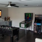 game room with tv mounted on a wall and pinball machines